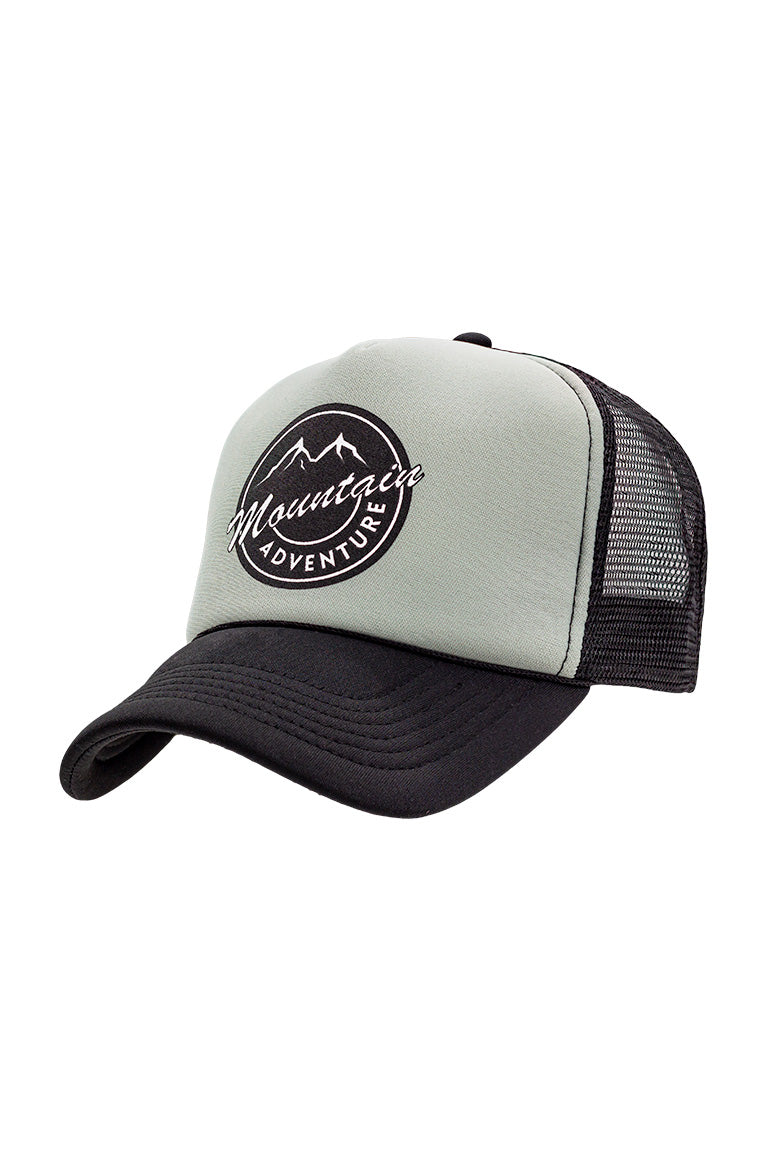 Front view of foam trucker hat with black visor and gray foam top. Breathable mesh in back of hat. Design on cap of a mountain inside a circle with the words mountain and adventure underneath.