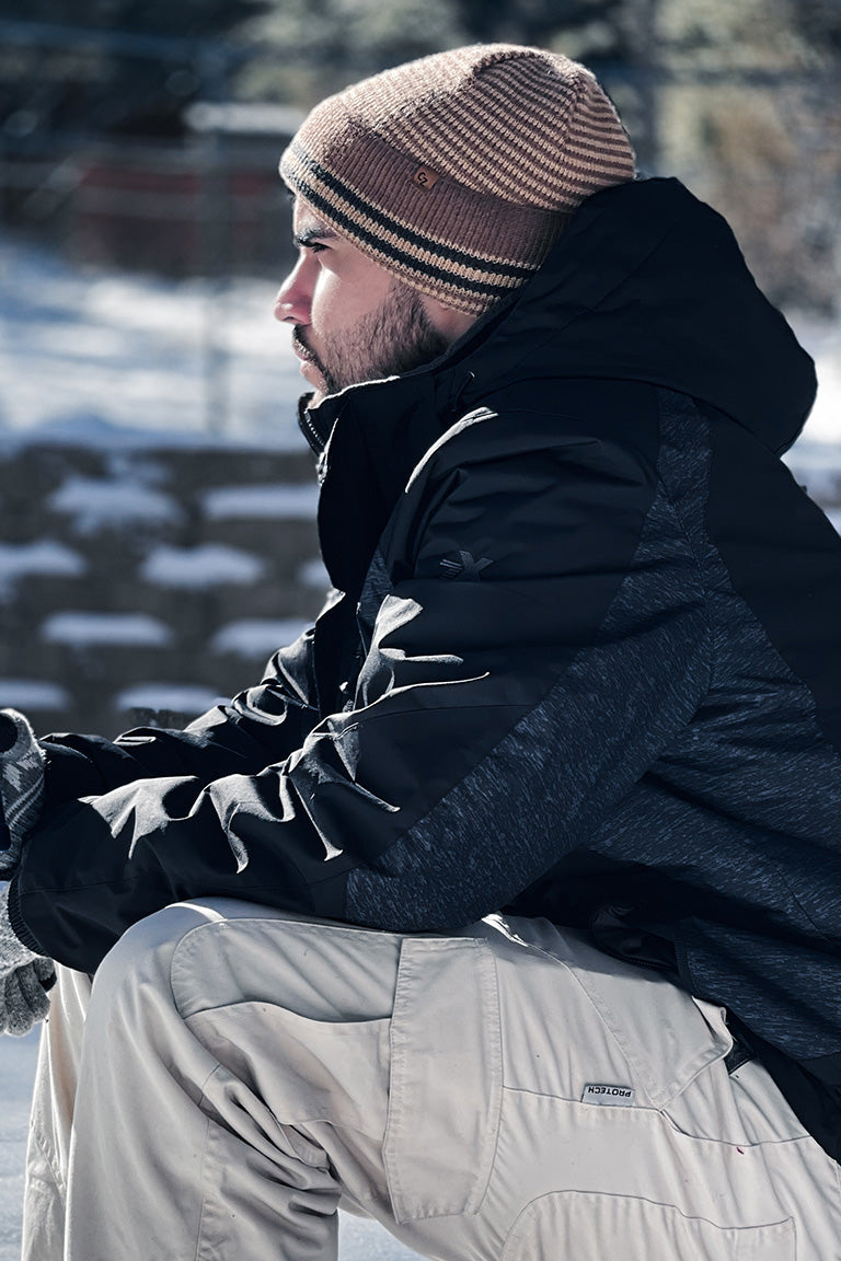 A photoshoot with a male model wearing winter clothes in the snow and a brown stripe beanie