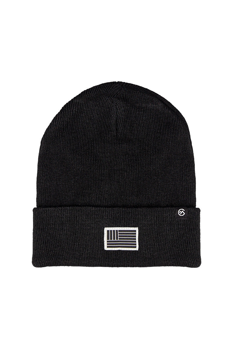 A black beanie with a small patch of a flag of black and white bars going horizontal with a small square at the top left of black and white bars going vertical