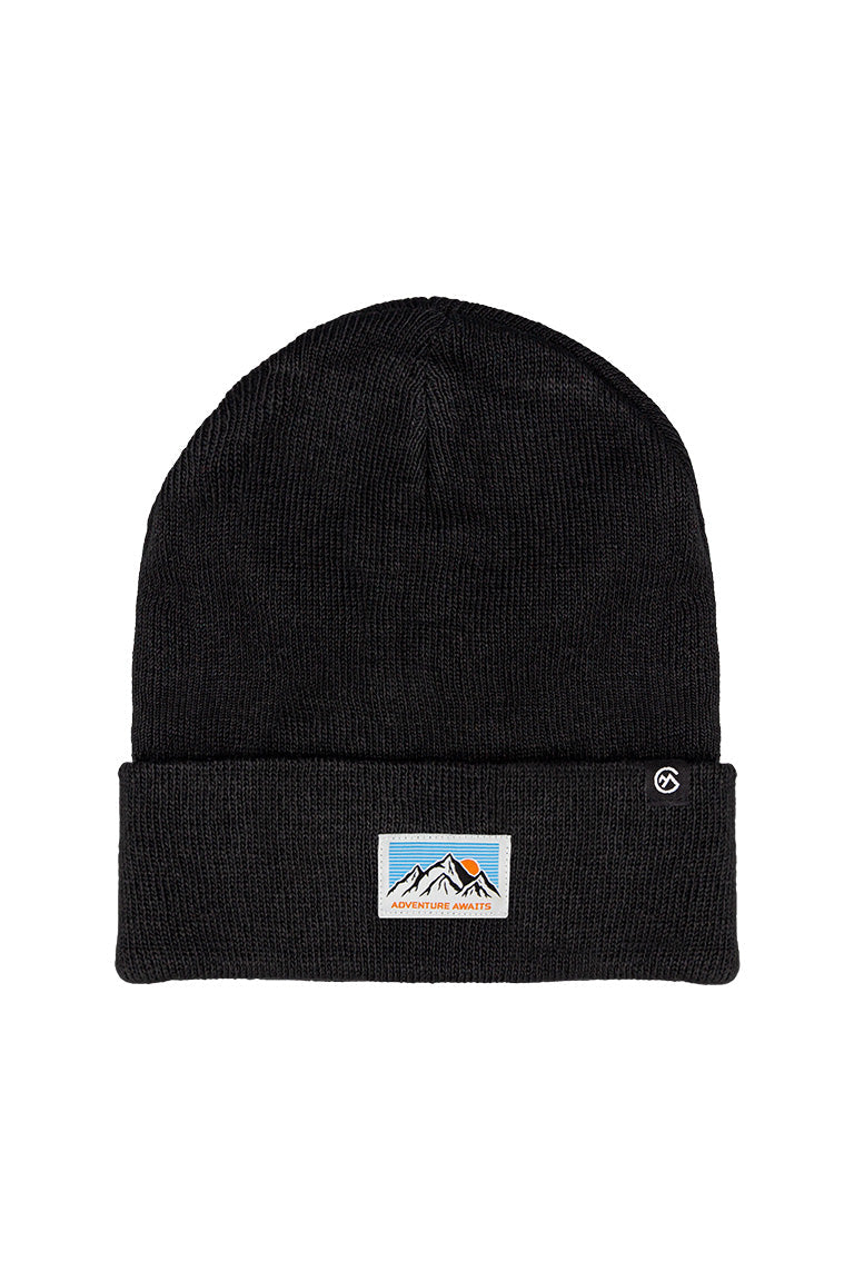 A black beanie with a small patch of a mountain design with a sunrise coming up behind on a blue sky. Has the text at the bottom "Adventure Awaits"
